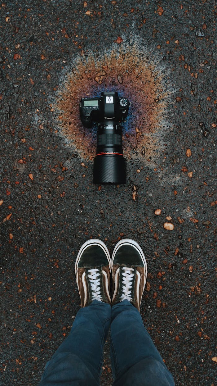 DSLR camera on wet pavement with colorful oil spill reflection, framed by sneakers.